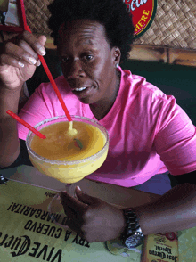 a woman in a pink shirt is drinking a margarita with a straw