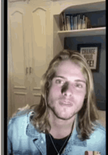 a young man with long blonde hair is standing in front of a wall with a sign that says change your life