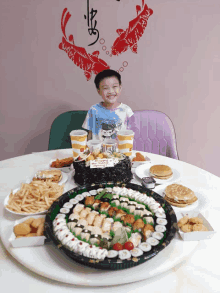 a young boy sits at a table with a birthday cake and a tray of food