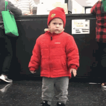 a little boy wearing a red jacket and a red hat is standing in front of a sign that says " homesick "