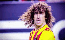 a soccer player with long curly hair is wearing a yellow and red striped shirt .