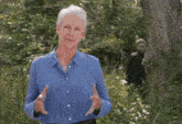 a woman in a blue shirt is standing in the woods holding a piece of wood in her hands .