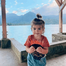 a little girl is standing next to a body of water .