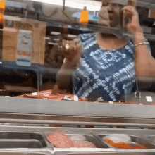 a woman in a blue and white tie dye shirt is standing in front of a display case of food