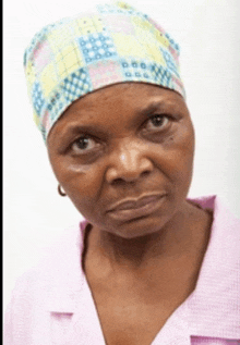 a woman wearing a pink shirt and a colorful hat looks at the camera with a sad look on her face