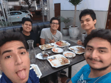 a group of young men are sitting at a table with plates of food on it