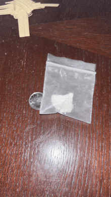 a bag of cocaine sits next to a quarter on a wooden table