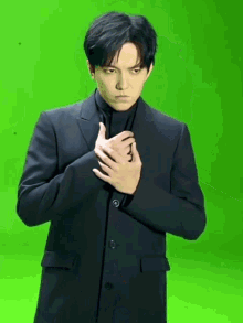 a man in a black suit holds his hands to his chest in front of a green screen