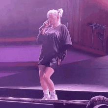 billie eilish is standing on a stage holding a microphone .