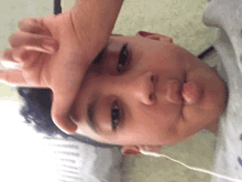 a young boy holds his hand to his forehead while wearing ear buds