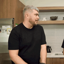 a man in a black shirt is standing in a kitchen with a sticker on the wall that says ' uber '