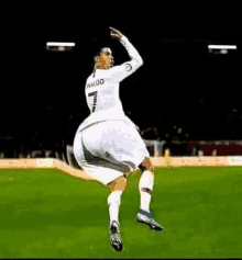 a soccer player is jumping in the air while wearing a white jersey with the number 7 on it .