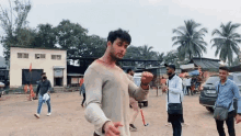 a man in a white shirt is standing in a dirt field with a group of people .