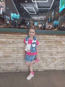 a little girl leaning against a brick wall in front of a restaurant with a sign that says ' armani ' on it