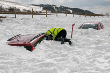 a red car is stuck in the snow and a man is digging it out with a shovel