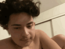 a shirtless man with curly hair is laying on a bed and looking at the camera .