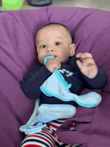 a baby wearing a shirt that says ' abercrombie & fitch ' on it chews on a blue blanket