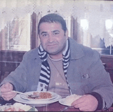 a man wearing a scarf with the letter a on it sits at a table eating food