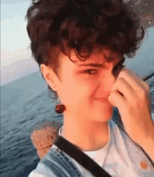 a young man with curly hair is taking a selfie by the ocean .