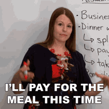 a woman standing in front of a white board with the words " i 'll pay for the meal this time " written on it