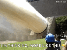 a man in a blue hard hat is standing in front of a large pipe that is coming out of a building .