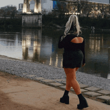 a woman in a black top and shorts is walking by a body of water with a bridge in the background