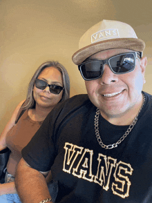 a man wearing a vans hat and sunglasses poses with a woman