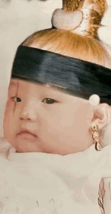 a baby is wearing a crown and earrings and looking at the camera .