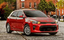 a red kia rio hatchback parked on a cobblestone street