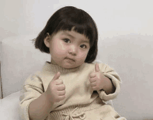 a little girl is sitting on a couch and giving a thumbs up .