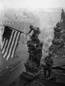 a black and white photo of soldiers on top of a building with an american flag in the foreground