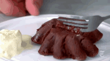 a person is holding a fork over a piece of red velvet cake on a plate with ice cream .