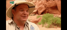 a man wearing a hat and a shirt with a triangle on it is standing in front of a rock wall .