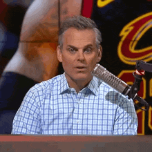 a man in a plaid shirt is sitting in front of a microphone with a cleveland cavaliers logo in the background