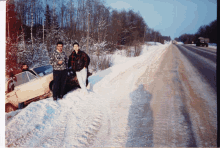 a group of people standing next to a car that has fallen into the snow