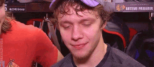 a young man wearing a hat and a black shirt is sitting in a locker room with his eyes closed .