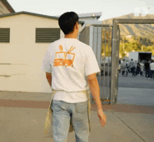 a man wearing a white t-shirt with a picture of a truck on the back is walking down a sidewalk .