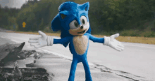 sonic the hedgehog is standing on a road with his arms outstretched .