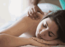 a woman laying on a bed getting a massage with her eyes closed