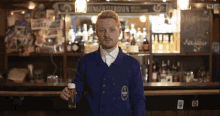 a man in a blue jacket holds a glass of beer in front of a sign that says ' weinkeller ' on it