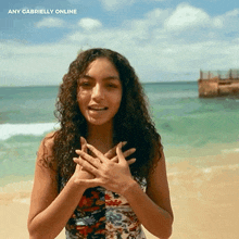 a woman standing on a beach with her hands on her chest and the words any gabrielly online behind her