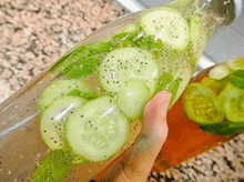 a person is holding a bottle of water with cucumber slices and mint leaves in it .