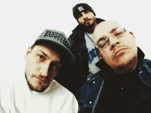 three men are posing for a picture and one of them is wearing a hat that says ' angels ' on it