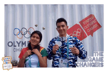 a man and a woman are posing for a picture in front of a sign that says youth olympic games