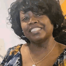 a woman with curly hair is smiling and wearing a necklace .