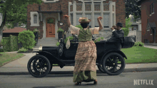 a woman in a green dress is dancing in front of an old car that says netflix on the side