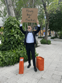 a man in a tuxedo is holding up a sign that says buy her a birkin