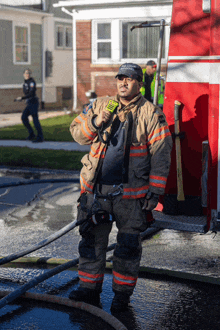 a man in a fireman 's uniform holds a walkie talkie while standing in front of a fire truck