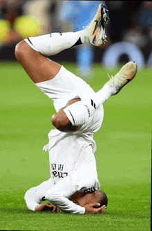 a soccer player wearing a fly emirates shirt is doing a handstand on the field