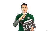 a man in a green shirt is holding a clapper board that says scene cut take and roll